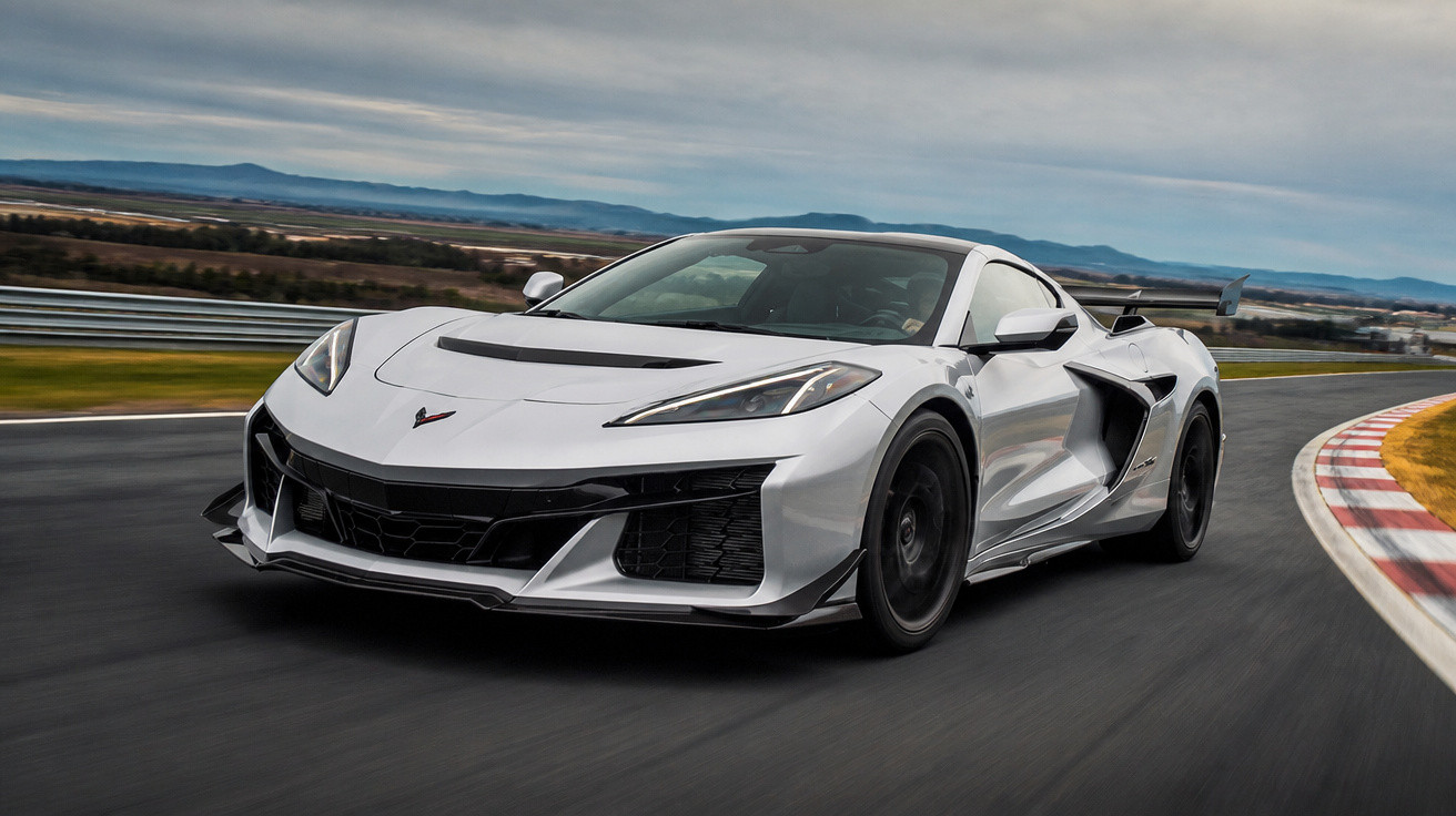 Carro esportivo branco em alta velocidade em pista de corrida com curva à direita e horizonte ao fundo.