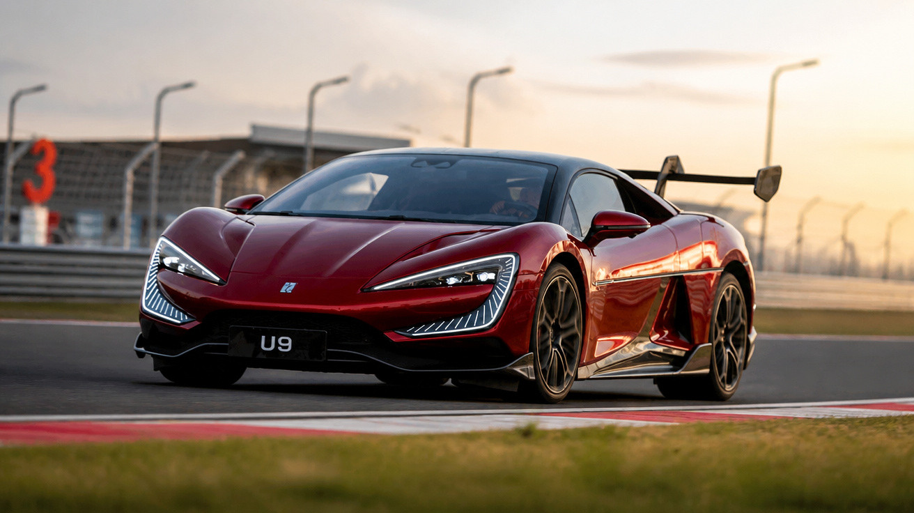 Carro esportivo vermelho em pista de corrida com aerofólio e luzes de LED acesas ao pôr do sol.