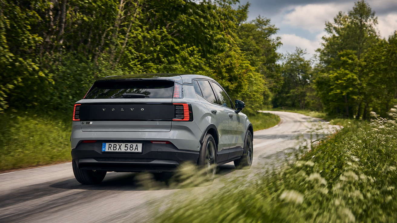 Carro Volvo XC40 cinza trafegando por estrada sinuosa cercada de árvores e vegetação verde.