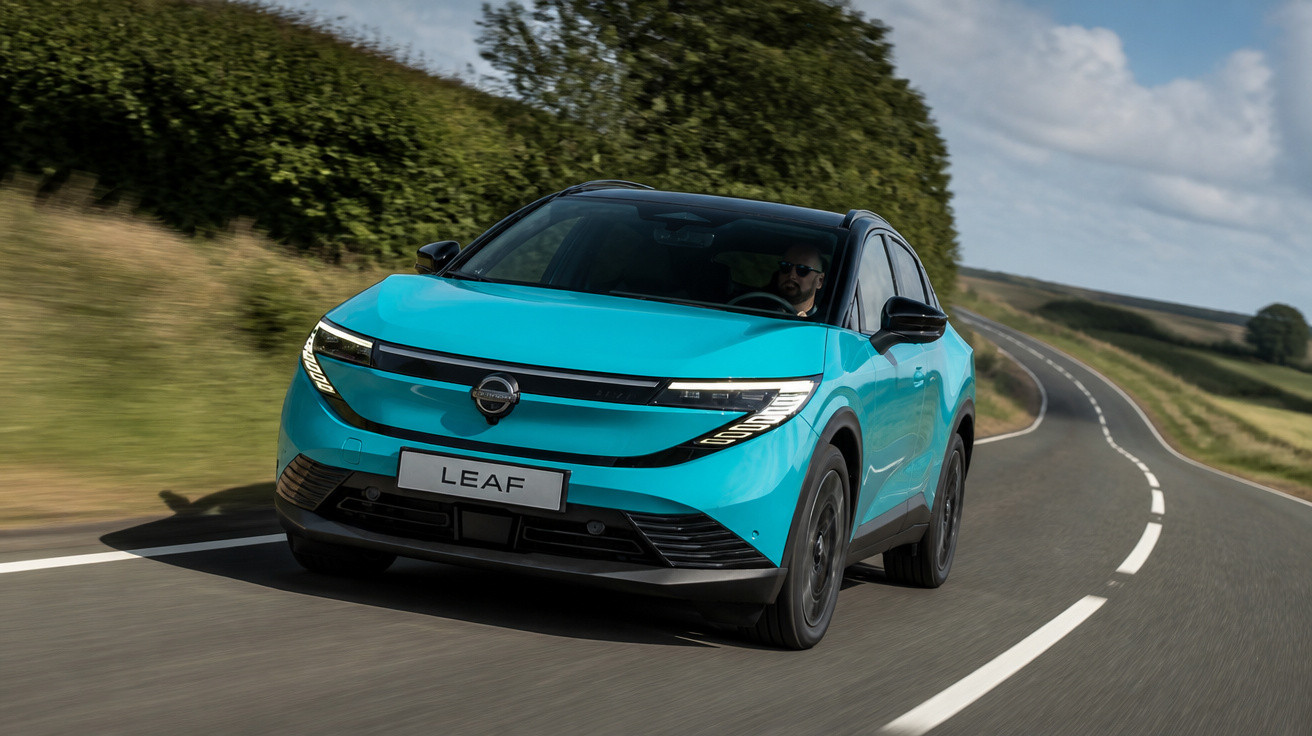 Carro azul elétrico Nissan Leaf trafegando em estrada rural sinuosa com céu parcialmente nublado.