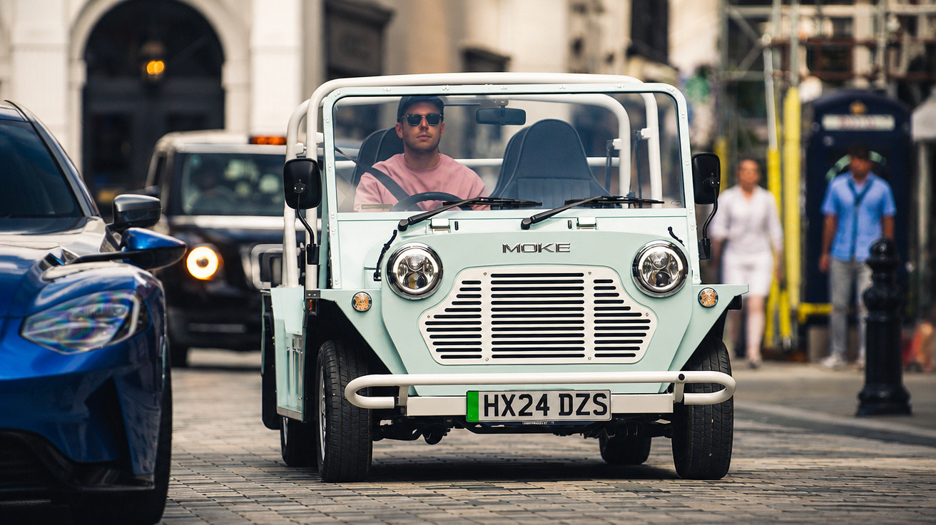 Homem de óculos escuros dirigindo carro conversível Moke branco em rua de paralelepípedo urbana.