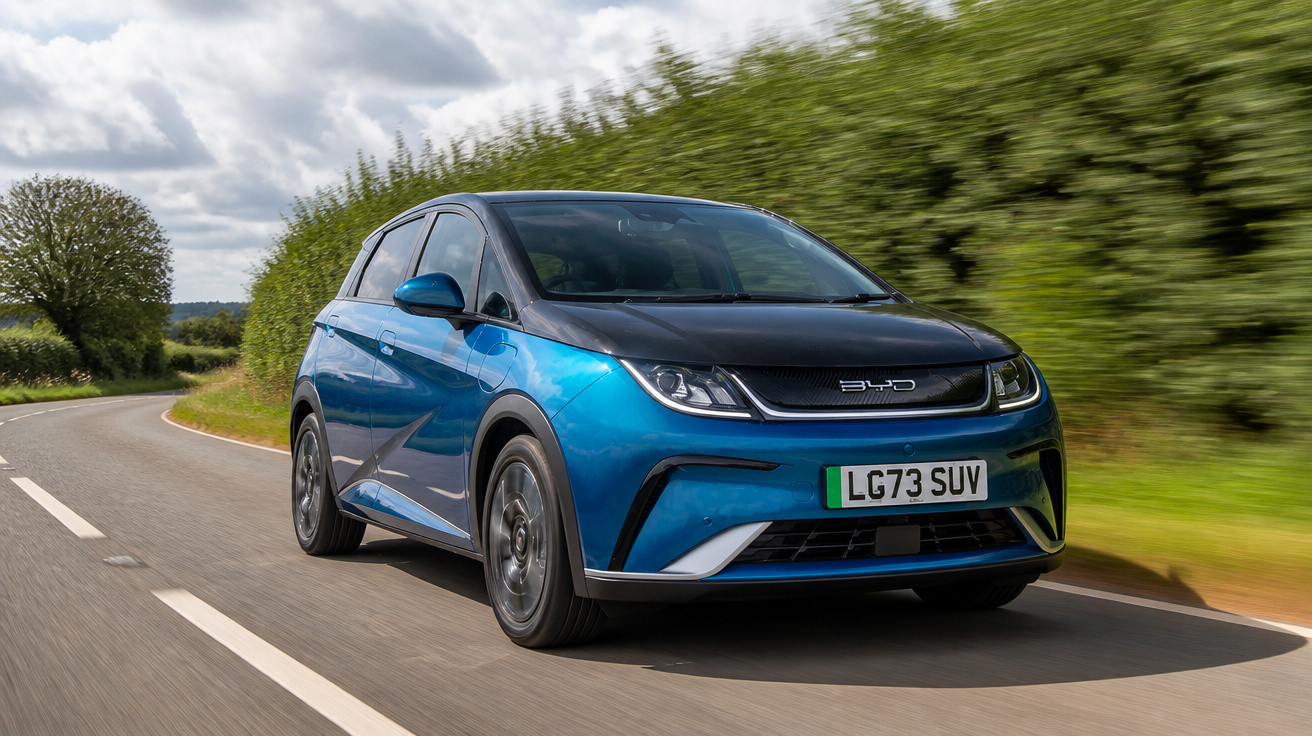 Carro elétrico azul BYD em estrada curva cercada por árvores e céu nublado.