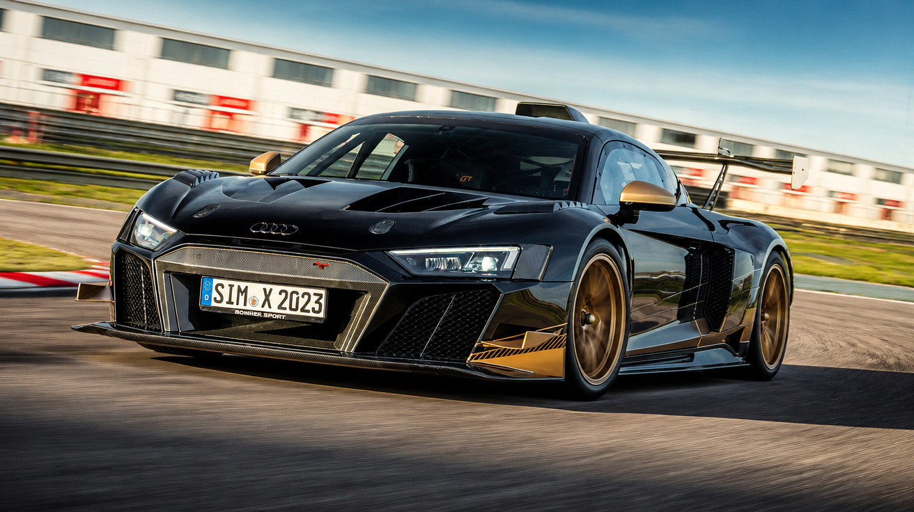 Carro esportivo Audi R8 preto com detalhes dourados em alta velocidade em pista de corrida.