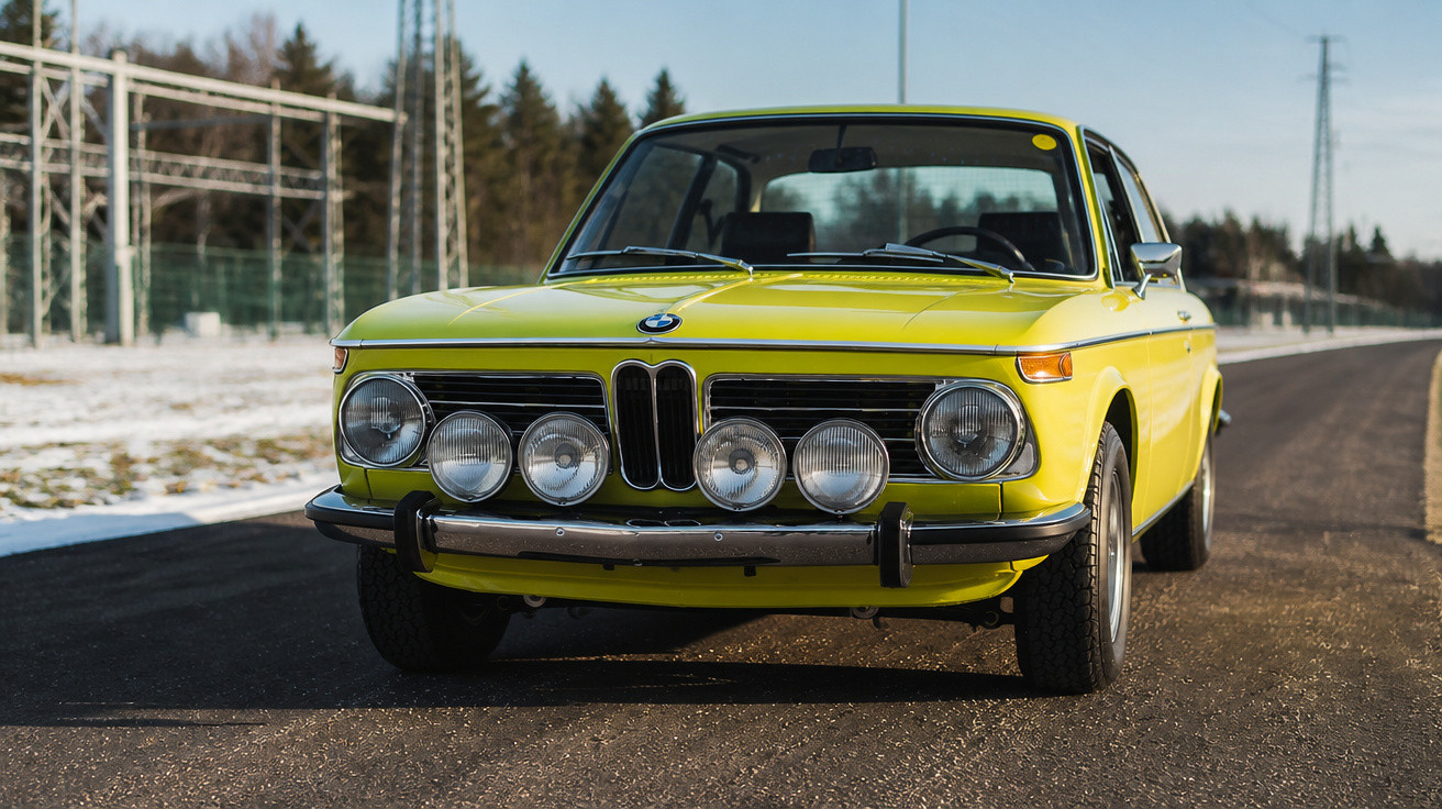 Carro BMW clássico amarelo estacionado em estrada asfaltada sob céu claro.