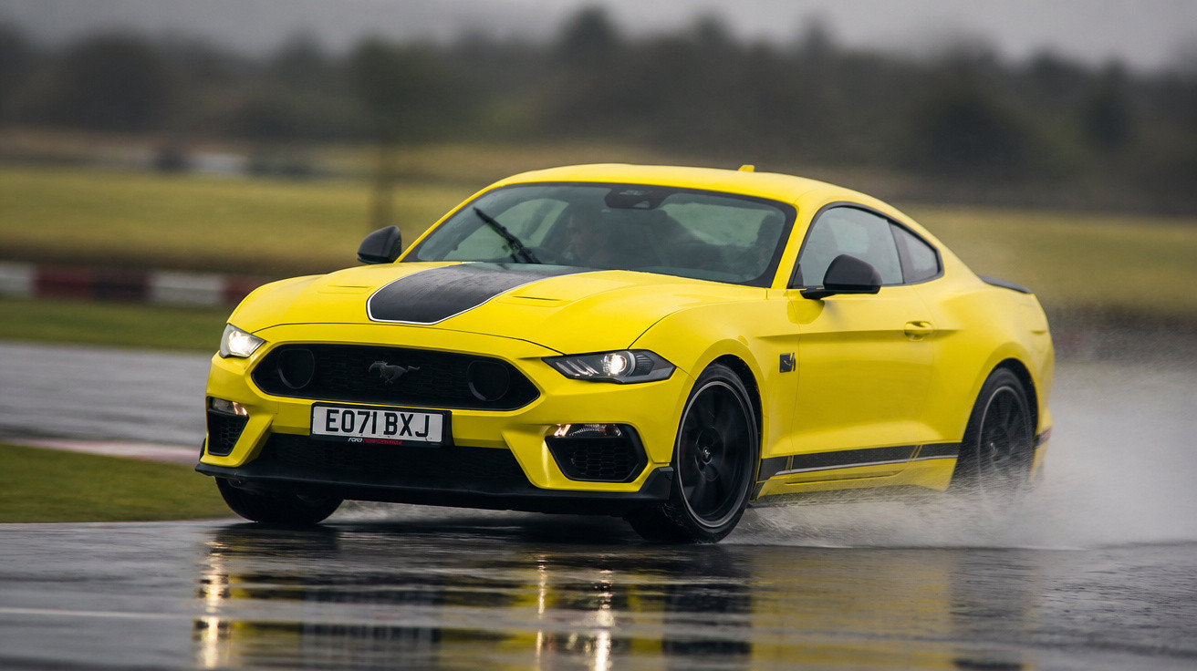 Carro esportivo amarelo Ford Mustang em pista molhada, criando respingos de água.