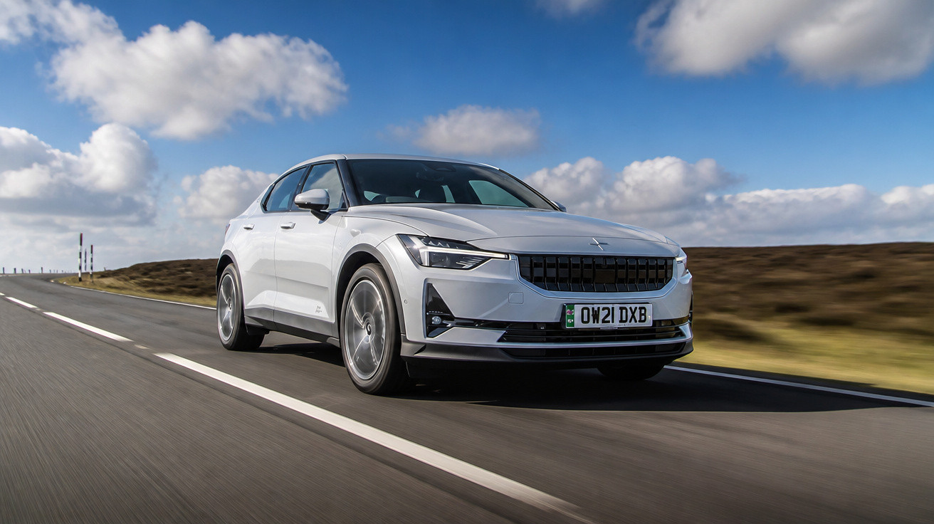 Carro elétrico branco Polestar 2 em movimento em estrada asfaltada sob céu azul com nuvens.