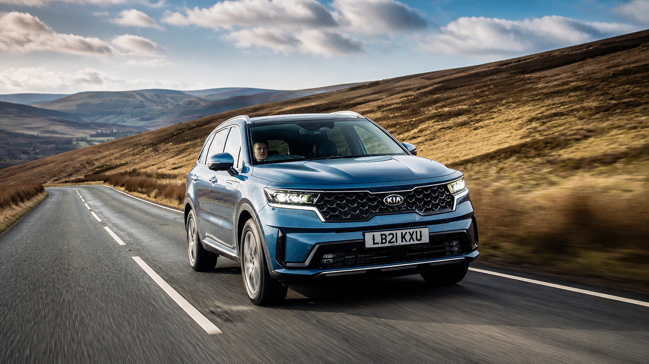 SUV azul da Kia modelo Sorento trafegando por estrada sinuosa em área rural montanhosa.