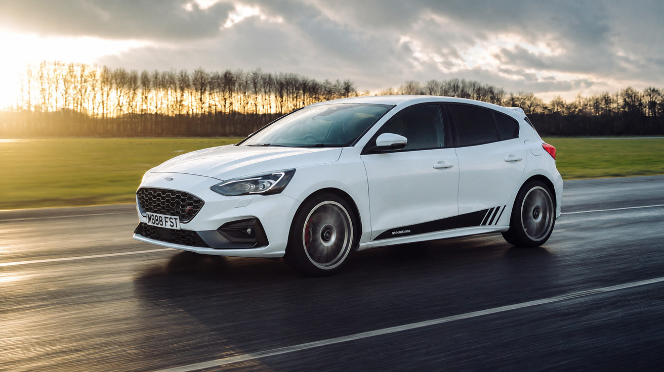 Carro branco hatchback em movimento em estrada molhada ao pôr do sol com árvores ao fundo.