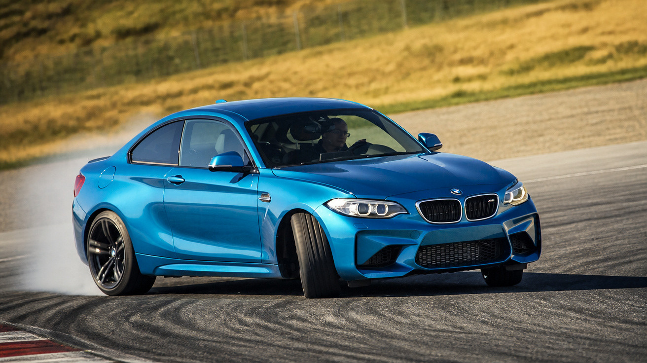 Carro esportivo BMW azul fazendo curva em pista de corrida com marcas de derrapagem no asfalto.